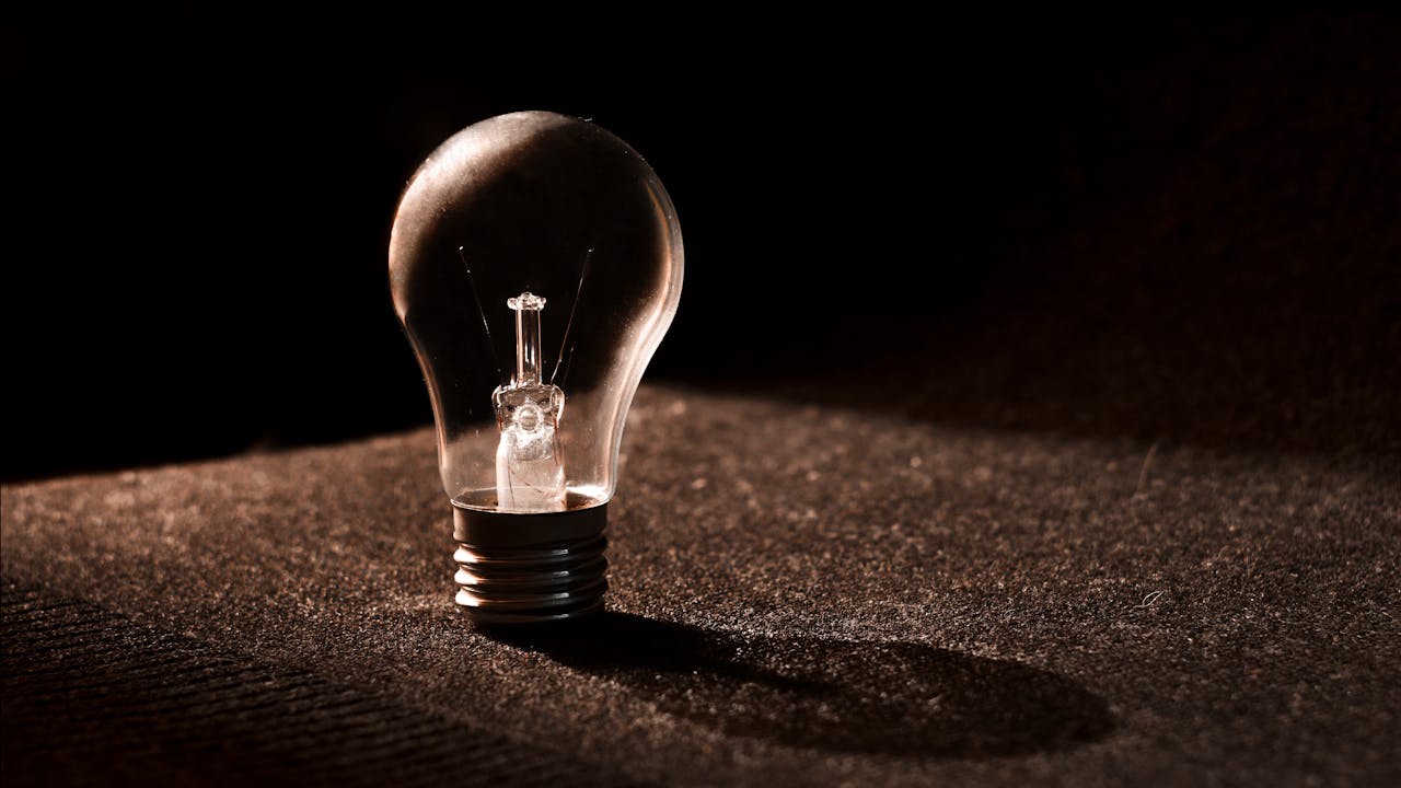 Close-up of a light bulb against a dark background, showcasing shadows and reflections.