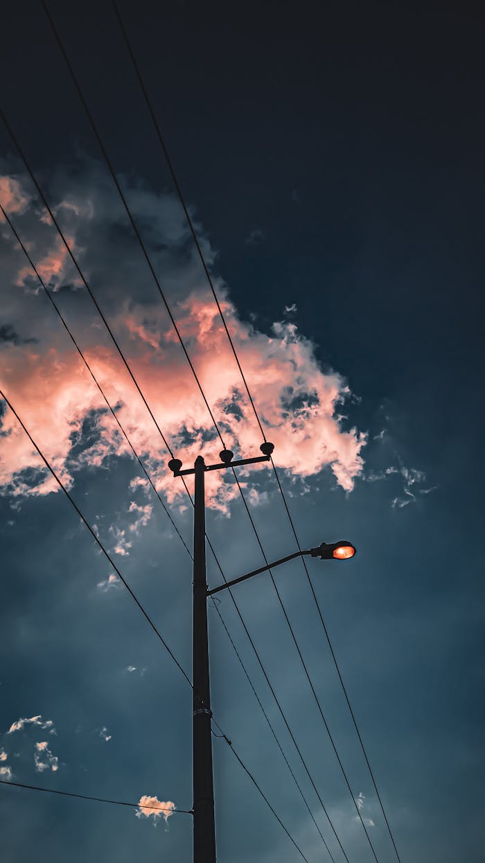 Silhouette of power lines and a pole against a vivid sunset sky with glowing clouds.